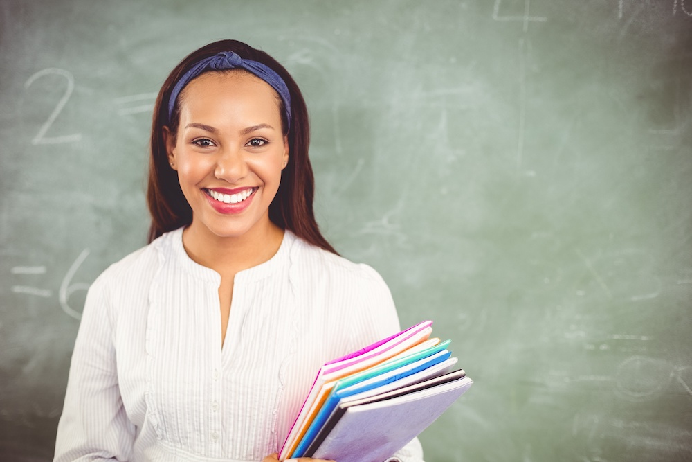 Portrait of smiling school teacher holding books in classroom